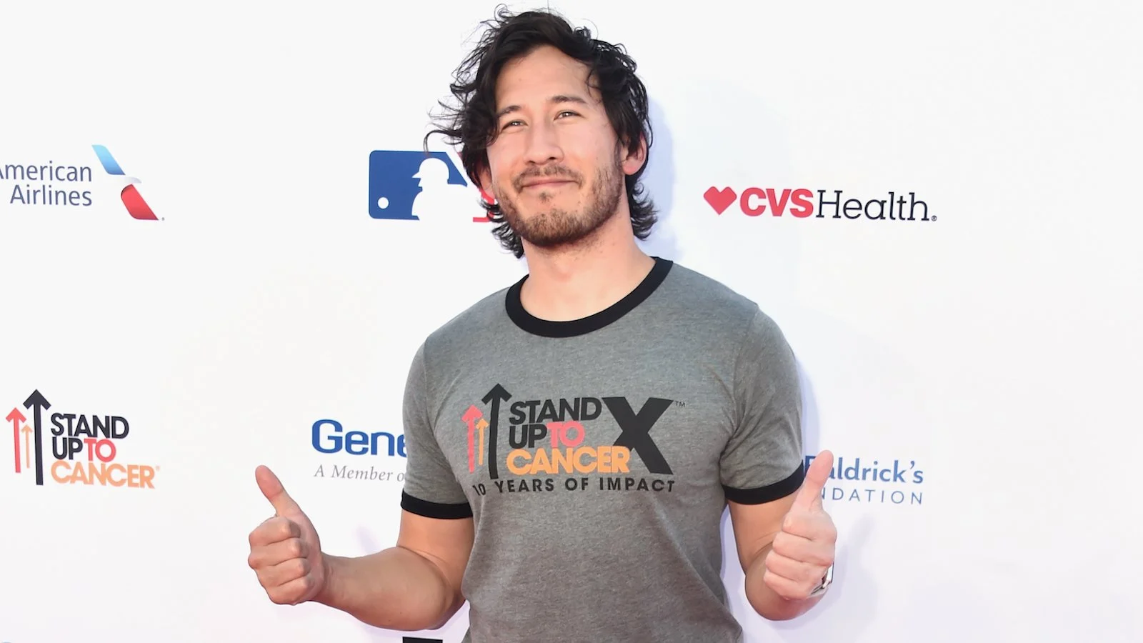 Mark Fischbach wearing a 'Stand up to Cancer' shirt holding his thumbs up